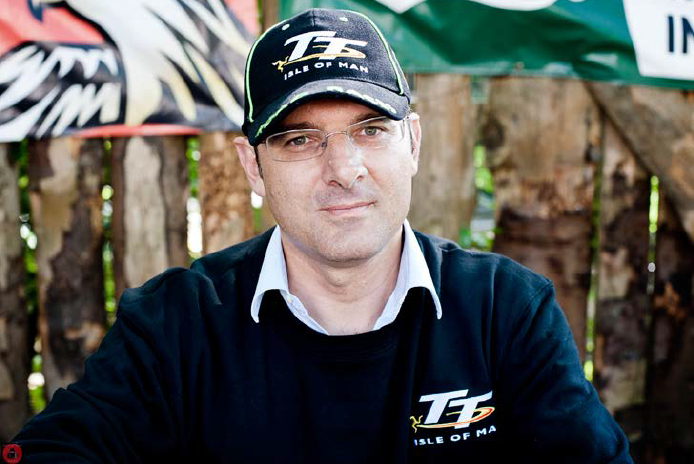 Carlo, production manager, sitting in the open air bar, looking straight to camera, with a TT isle of man baseball cap on.
