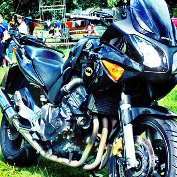 A black motorcycle sporting a half fairing and a Batman sticker, parked at a festival.