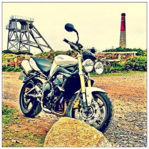 A Triumph street fighter parked in on gravel near the winding gear of a mine.