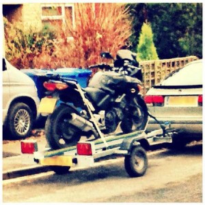 The black bike strapped onto a bike trailer, hooked onto the back of a Saab.