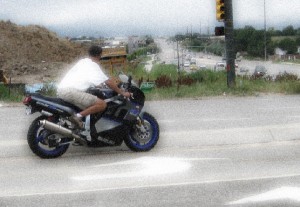 A guy riding a race replica sports bike wearing shorts, t-shirt, sandals and no helmet or gloves on a summer evening