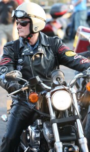 A quite middle aged biker on a Harley, wearing leathers, an open face helmet,  and dark glasses.