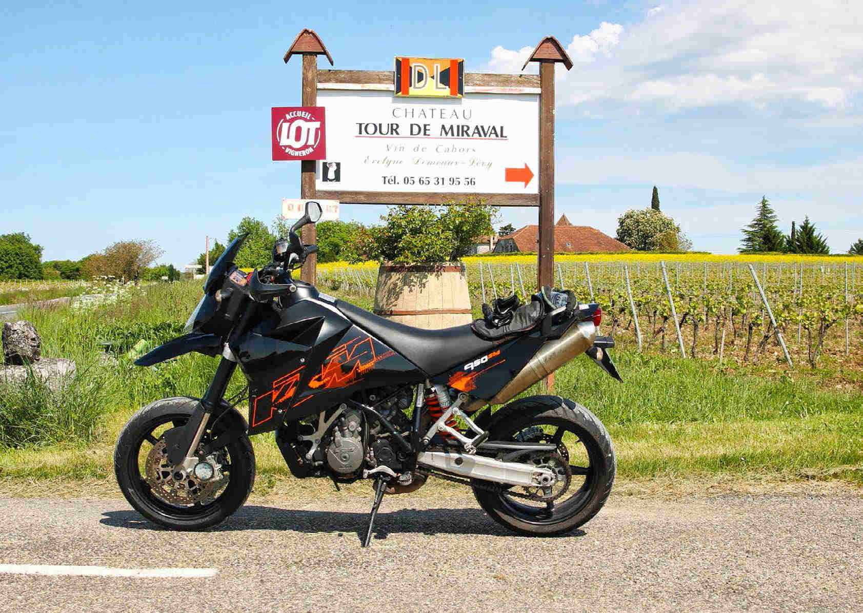 Side view of the KTM, parked on the road, below a sign for the Chateau Tour De Miraval