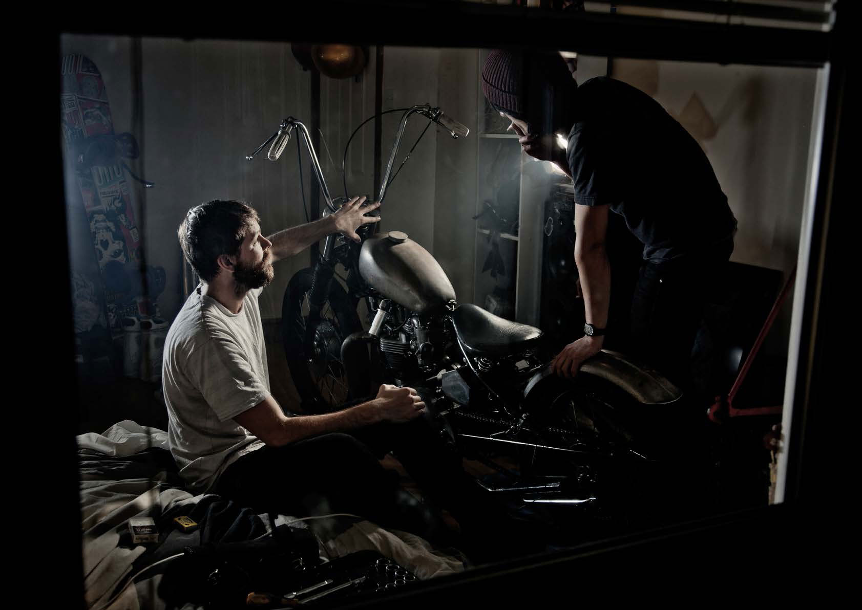 Two young men discussing a motorcycle chopper parked in their bedroom.