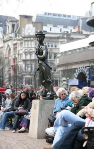 People sitting on benches in London next to a statue of Charlie Chaplin