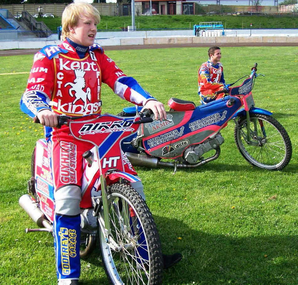 Lad sitting on a speedway bike, in front of another parked bike in the middle of the stadium